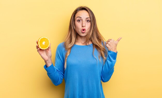 Mooie vrouw die verbaasd in ongeloof kijkt en half oranje vasthoudt