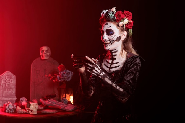 Mooie vrouw die videogames speelt op smartphone, met behulp van mobiele telefoon op de dag van de dode halloween-viering. La cavalera catrina heeft plezier op heilig mexicaans festival, griezelige vakantie.