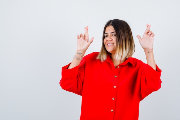 Mooie vrouw die vingers gekruist houdt in rode blouse en er gelukkig uitziet. vooraanzicht.