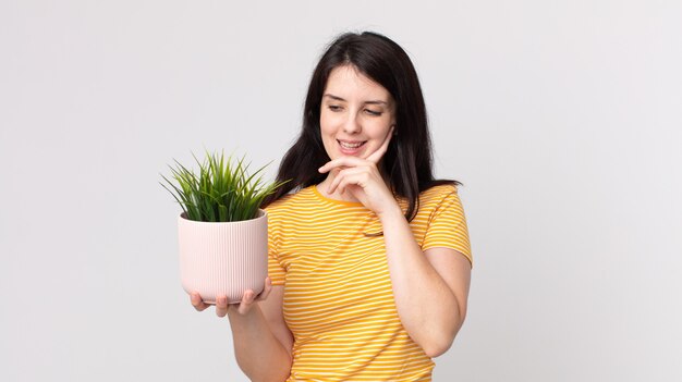 Mooie vrouw die vrolijk lacht en dagdroomt of twijfelt en een decoratieve plant vasthoudt