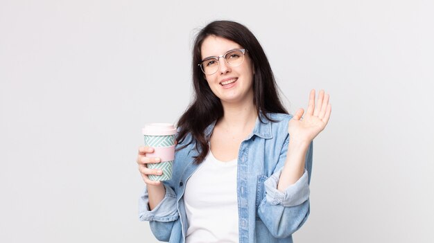 Mooie vrouw die vrolijk lacht, met de hand zwaait, je verwelkomt en begroet en een afhaalkoffie houdt