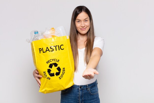 Mooie vrouw die vrolijk lacht met een vriendelijke, zelfverzekerde, positieve blik, een object of concept aanbiedt en toont