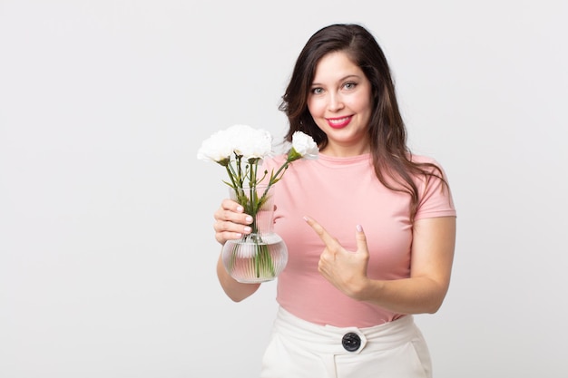 Mooie vrouw die vrolijk lacht, zich gelukkig voelt en naar de zijkant wijst en een decoratieve bloemenpot vasthoudt