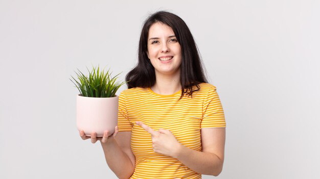 Mooie vrouw die vrolijk lacht, zich gelukkig voelt en naar de zijkant wijst en een decoratieve plant vasthoudt