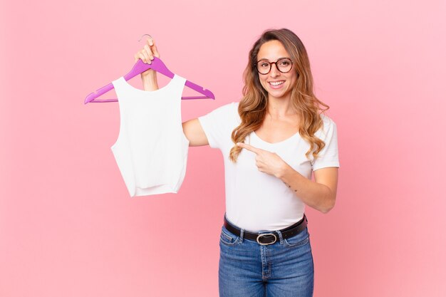 Mooie vrouw die vrolijk lacht, zich gelukkig voelt en naar de zijkant wijst en kleding kiest