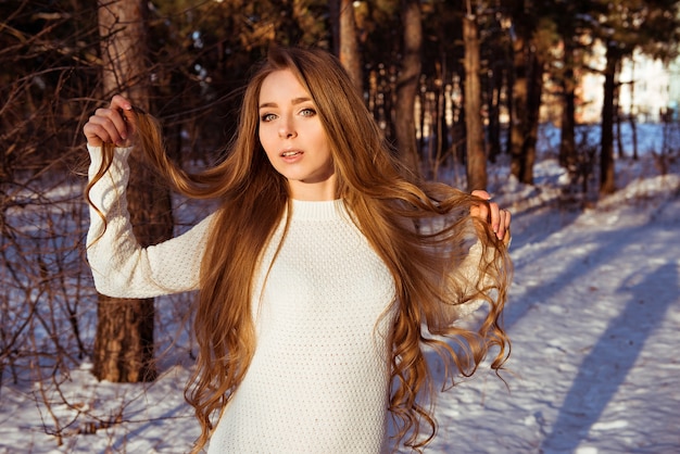 Mooie vrouw die witte sweater draagt die haar krullen in de winterbos houdt