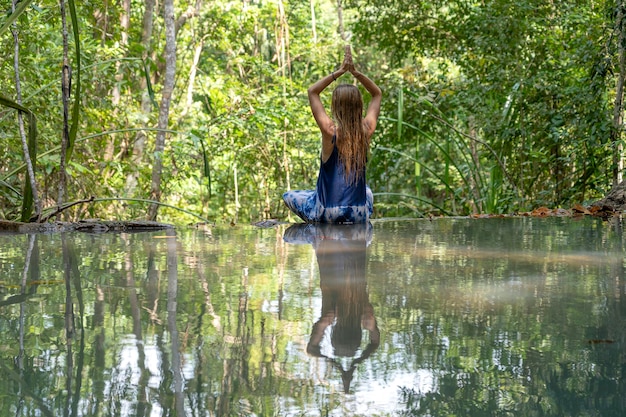 Mooie vrouw die yoga beoefent in de buurt van turkoois water van de cascadewaterval op het diepe tropische regenwoudeiland Koh Phangan Thailand