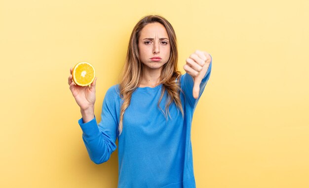 mooie vrouw die zich boos voelt en duimen naar beneden laat zien terwijl ze half oranje houdt