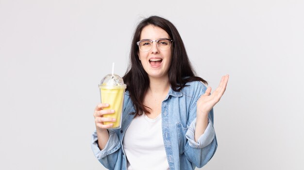 Mooie vrouw die zich gelukkig en verbaasd voelt over iets ongelooflijks en een vanillemilkshake vasthoudt