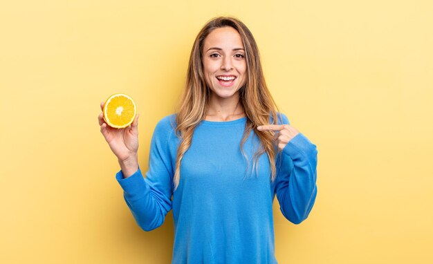 Mooie vrouw die zich gelukkig voelt en naar zichzelf wijst met een opgewonden half oranje vasthoudend