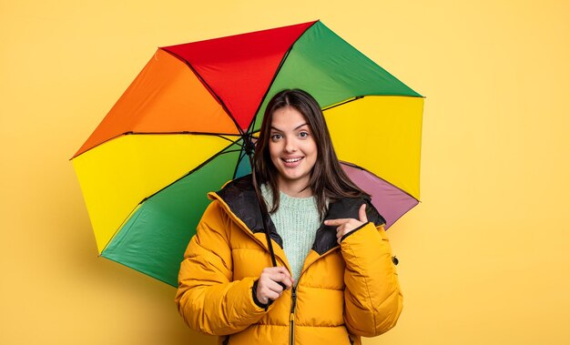 Mooie vrouw die zich gelukkig voelt en naar zichzelf wijst met een opgewonden winter en paraplu concept