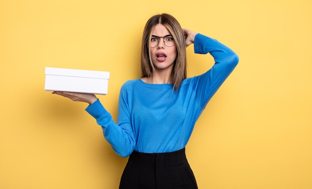 Mooie vrouw die zich gestrest, angstig of bang voelt met de handen op het hoofd met een witte doos