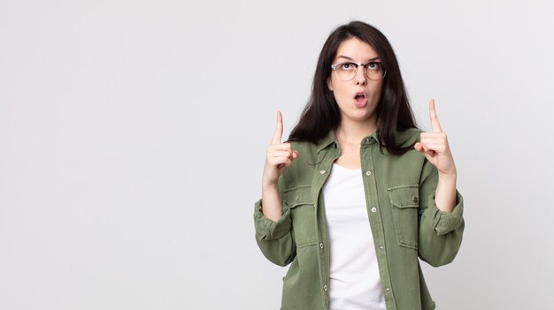 Mooie vrouw die zich onder de indruk voelt en met open mond naar boven wijst met een geschokte en verbaasde blik