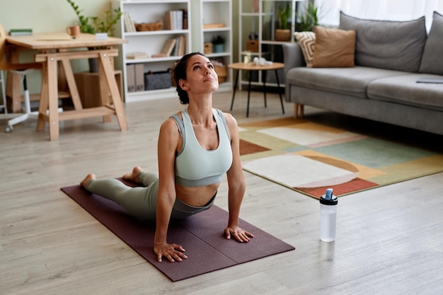 Mooie vrouw die zich uitstrekt op yoga mat genieten van training thuis