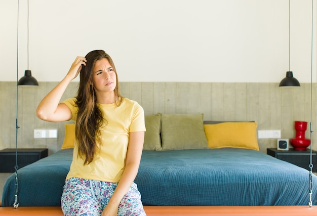 Mooie vrouw die zich verbaasd en verward voelt, haar hoofd krabt en naar de zijkant kijkt