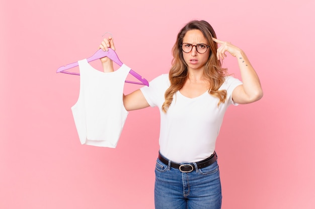 Mooie vrouw die zich verward en verbaasd voelt, laat zien dat je gek bent en kleding kiest