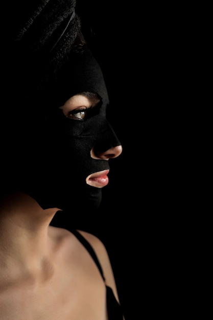 Mooie Vrouw die Zwart Gezichtsmasker toepast. Schoonheidsbehandelingen. Het close-upportret van Kuuroordmeisje past Clay Facial-masker op zwarte achtergrond toe