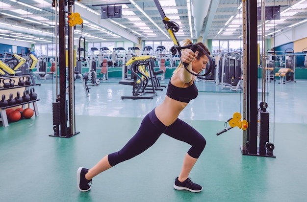 Mooie vrouw doet harde schorsing training met fitness bandjes in een fitnesscentrum. Gezond en sportief levensstijlconcept.