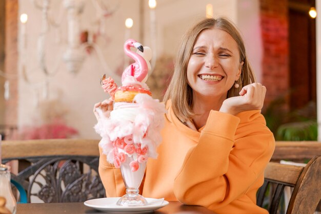 Foto mooie vrouw eet dessert in de vorm van roze flamingo in het café tijd voor plezier geloften in een heldere sweatshirt