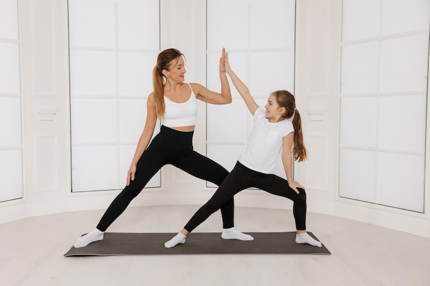 Mooie vrouw en haar charmante dochter glimlachen terwijl ze samen yoga doen