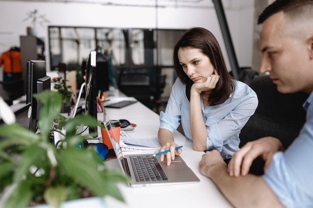 Mooie vrouw en jongen gekleed in kleding in kantoorstijl werken samen met laptop aan bureaus in het lichte moderne kantoor