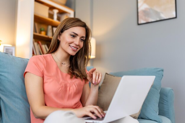 Mooie vrouw freelancer die informatie noteert voor het plannen van een project die afstandswerk doet via een laptop. Vrouw die lacht terwijl ze e-mail leest op een modern laptopapparaat.