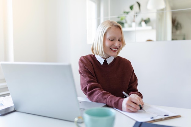 Mooie vrouw freelancer die informatie noteert voor het plannen van een project op afstand via laptop