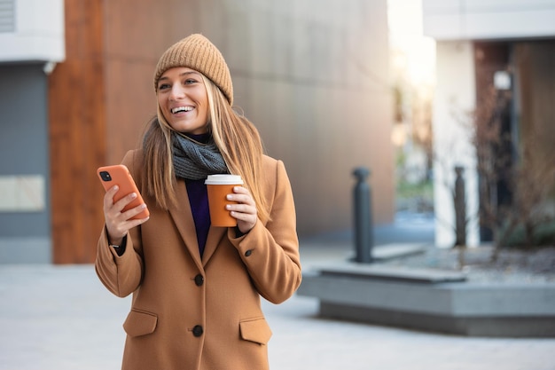 Mooie vrouw gaat werken met koffie wandelen in de buurt van kantoorgebouw Portret van succesvolle zakenvrouw met kopje warme drank