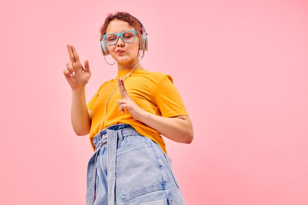 Mooie vrouw gele t-shirt hoofdtelefoon entertainment muziek plezier roze achtergrond ongewijzigd