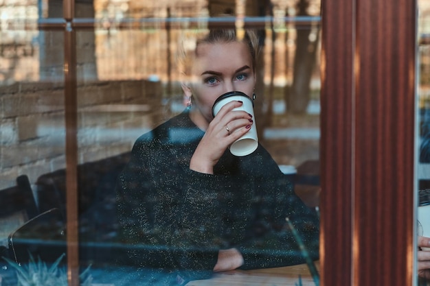 Mooie vrouw geniet van haar koffie terwijl ze in café bij het raam zit.