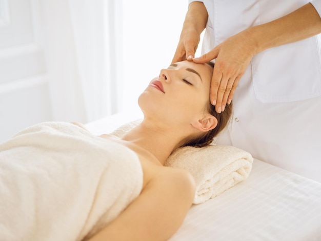 Mooie vrouw genieten van gezichtsmassage met gesloten ogen. Spa-behandelingsconcept in de geneeskunde.