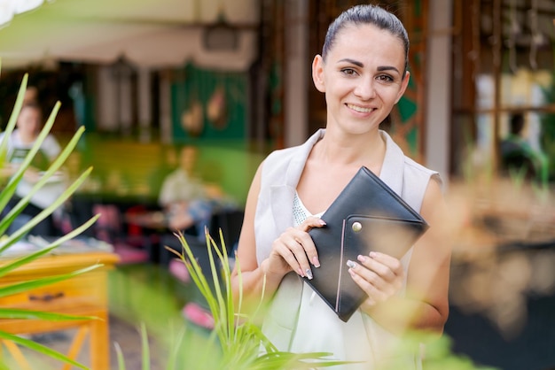 Mooie vrouw glimlachend gelukkig staande bij de stad notitieblok in de hand staande