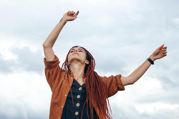 Mooie vrouw in boho-kleding met rode dreadlocks danst op de daken en ademt frisse lucht.