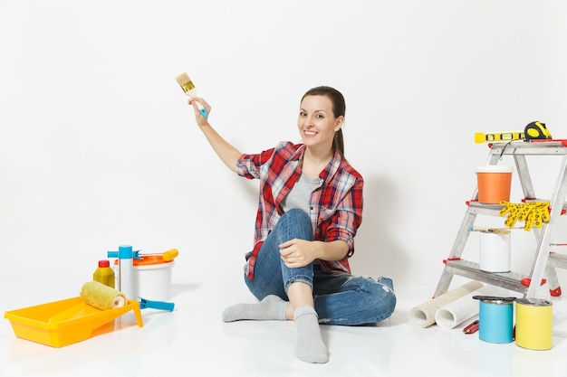 Mooie vrouw in casual kleding zittend op de vloer met borstel, instrumenten voor renovatie appartement kamer geïsoleerd op een witte achtergrond. Behangaccessoires voor het lijmen van tekengereedschappen. Reparatie thuis concept