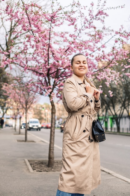 Mooie vrouw in de buurt van sakura bomen. Roze bloemen bloeien in de bomen op een stadsstraat. Rondom bloeien bomen. Lentetijd concept