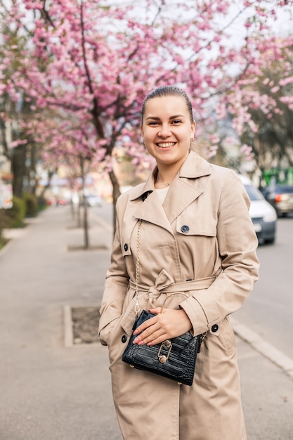 Mooie vrouw in de buurt van sakura bomen. Roze bloemen bloeien in de bomen op een stadsstraat. Rondom bloeien bomen. Lentetijd concept