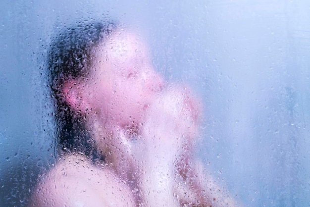 Mooie vrouw in de douche achter glas met druppels blauwe gloed