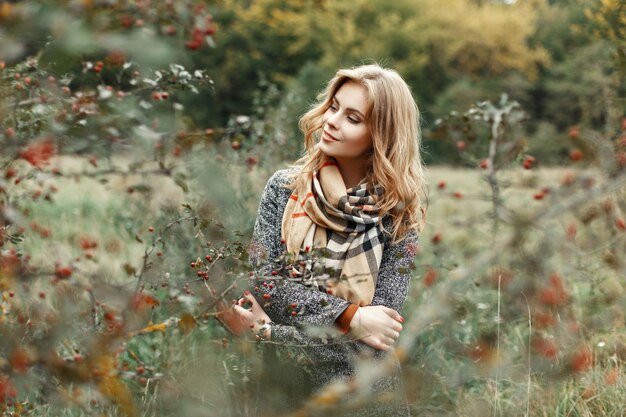 Mooie vrouw in de herfstkleren die in de tuin stellen.