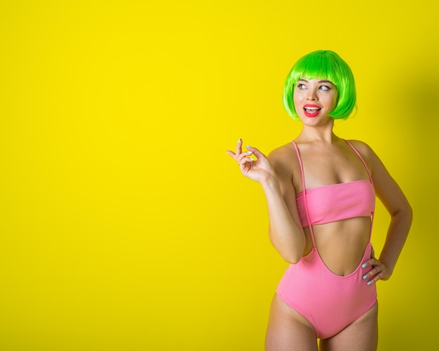 Mooie vrouw in een groene korte pruik en roze bikini poseren op een gele achtergrond Portret van een meisje met sensuele rode lippen