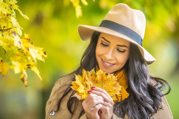 Mooie vrouw in een hoed houdt gele esdoornbladeren vast tijdens de herfst in de natuur.