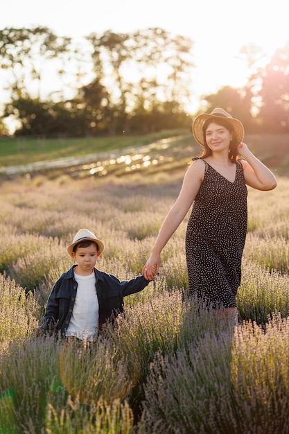 Mooie vrouw in een jurk en hoed loopt met haar zoon aan de hand in een lavendelveld