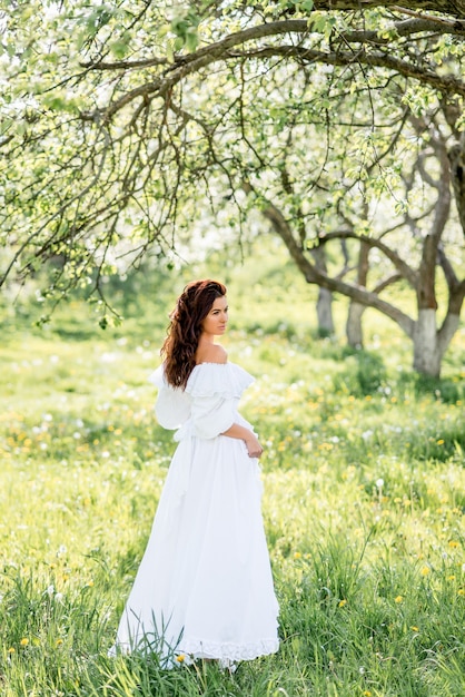 Mooie vrouw in een lange witte jurk in een lentetuin. Een meisje in een bloeiende tuin.