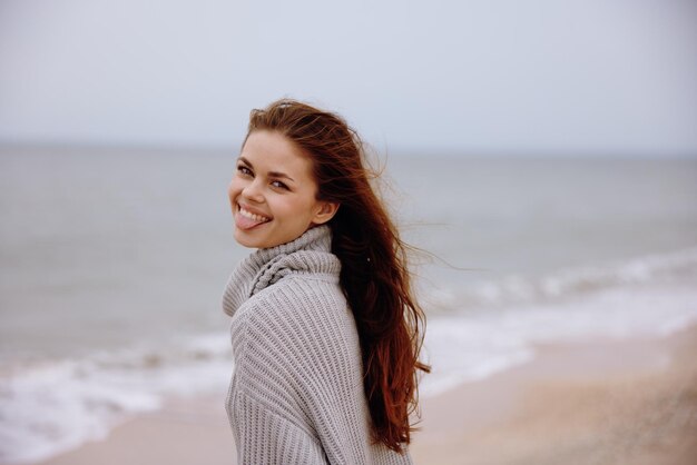 Mooie vrouw in een trui met vliegend haar bij de oceaan toerisme ontspanningsconcept foto van hoge kwaliteit