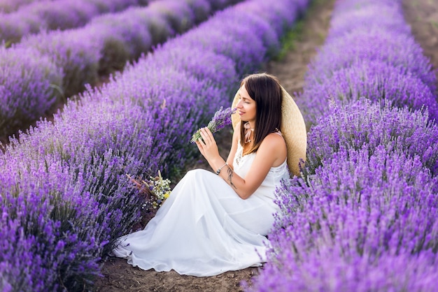 Mooie vrouw in een witte jurk en hoed verzamelt lavendel. Zomerfoto's.