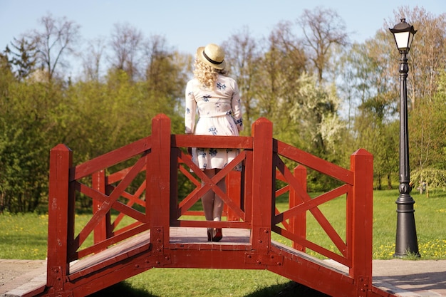 Mooie vrouw in een witte zomerjurk en een strohoed staat op een berkenbrug in het park