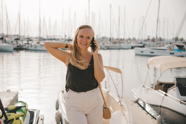 Mooie vrouw in gesprek aan de telefoon tegen de achtergrond van de blauwe zee en jachten