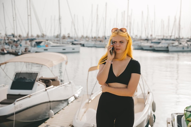 Mooie vrouw in gesprek aan de telefoon tegen de achtergrond van de blauwe zee en jachten