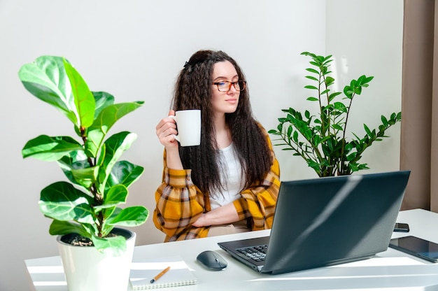 Mooie vrouw in glazen drinkt koffie tijdens een pauze op de werkplek Vrouw die thuis werkt met behulp van laptop