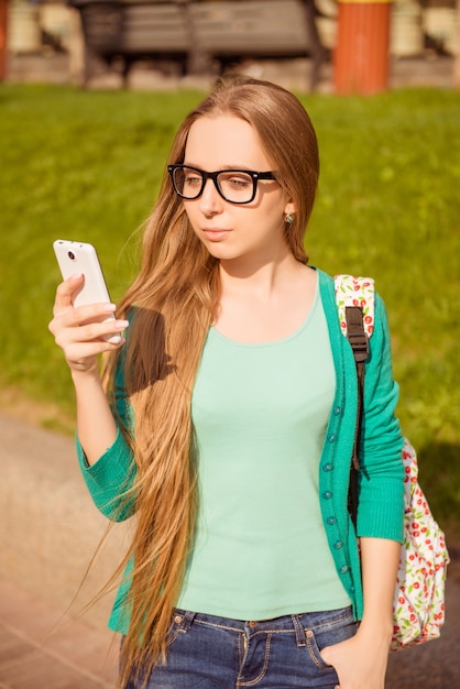 Mooie vrouw in glazen lopen en kijken naar haar mobiele telefoon