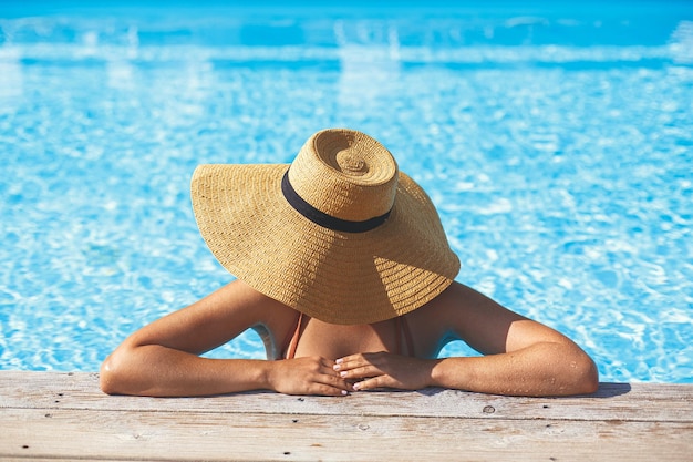 Mooie vrouw in hoed ontspannen bij zwembad pier in water genieten van zomervakantie in tropisch resort